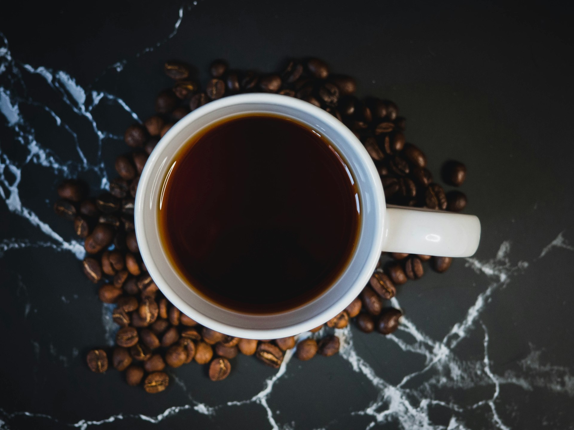 A freshly brewed espresso served in a white cup, surrounded by high-quality coffee beans on a marble countertop.
