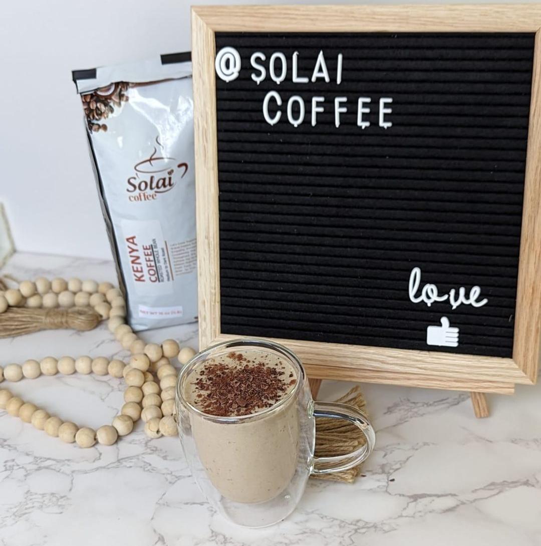 An image showing a framed Solai coffee positive vibe poster and freshly made coffee smoothie, Gen Z's preferred coffee drink, with a pack of Solai coffee Kenya specialty coffee behind it. 