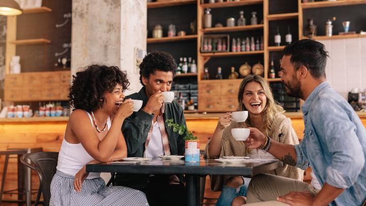 A picture showing younger coffee drinkers, millennials in a vibrant coffee shop scene engaged in lively conversations over cups of coffee.