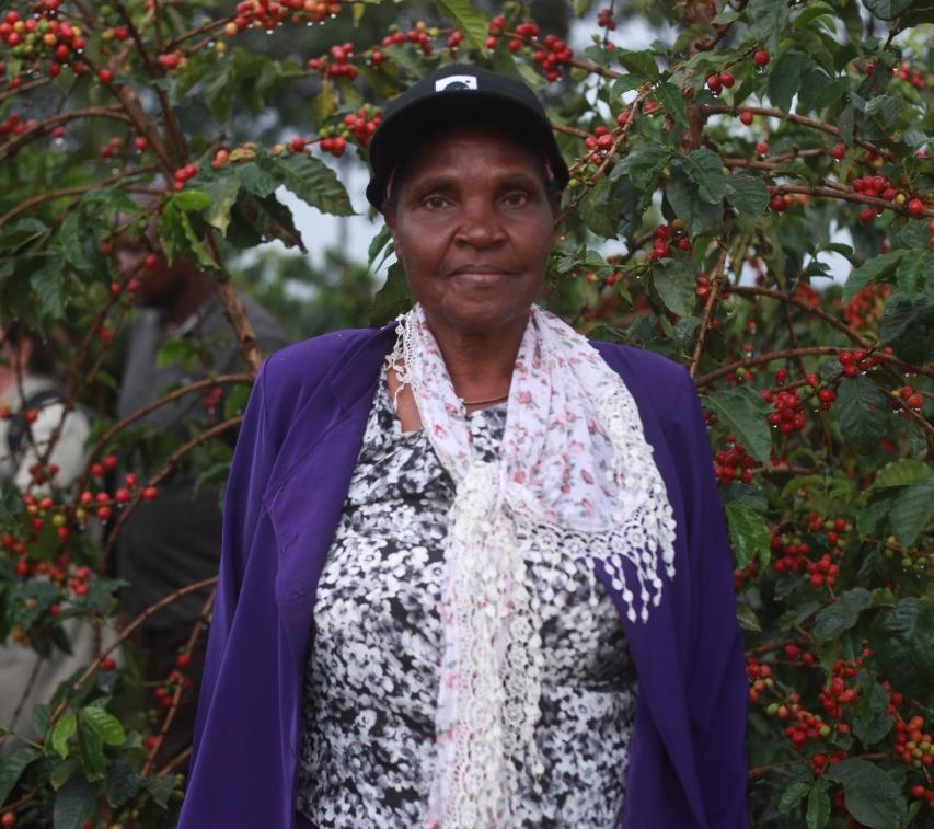 An image showing Margaret, Liwani coffee farm owner, posing for a photo in front of a coffee tree 