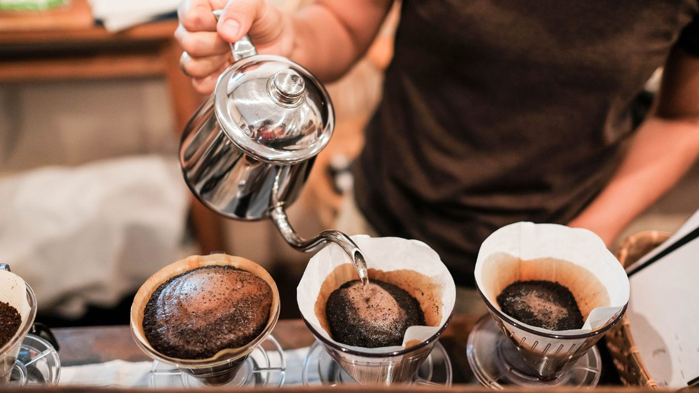 A person pours hot water into fresh coffee grounds, giving it time for a steeping period.