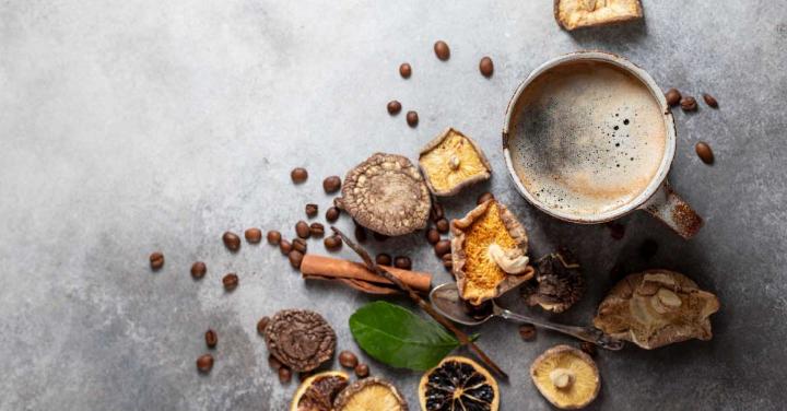 An image showing freshly brewed mushroom coffee on the surface includes coffee beans, mushrooms, and cinnamon.