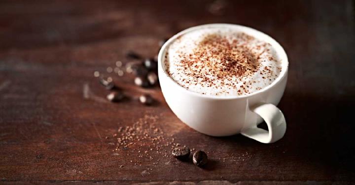 An image shows a cup of cocoa-infused coffee brew, with coffee beans and cocoa powder scattered on the surface.