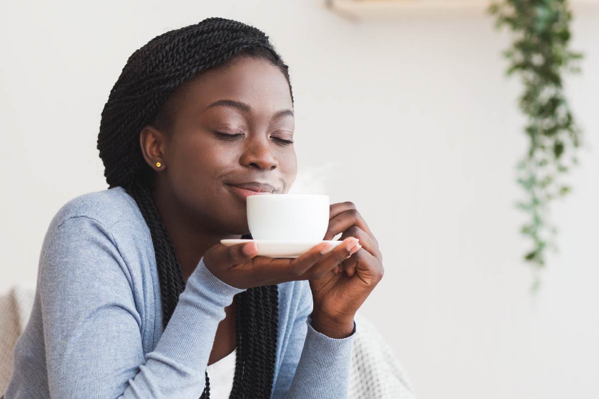 Woman savoring coffee with eyes closed, smiling—Cup's warmth, aroma, and taste in focus.