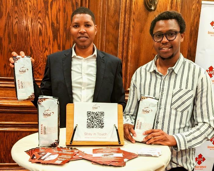 Peter Kuria, founder of Solai Coffee, confidently presents a selection of Solai Coffee products. Standing beside him is a participant in the 'Daring Abroad' program.