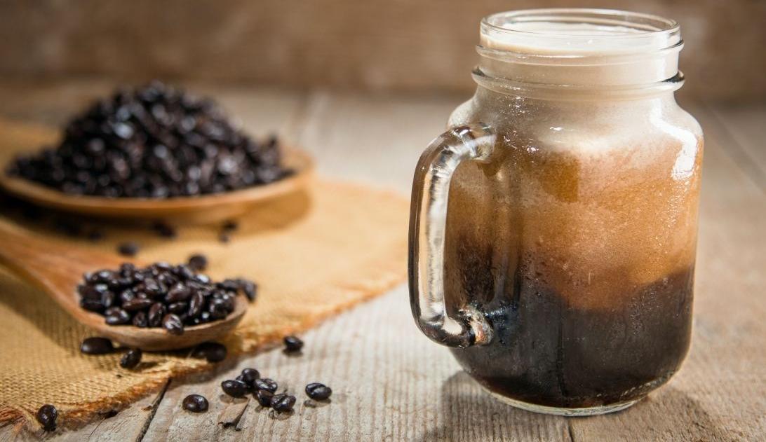 Nitro cold brew served in a glass mug on a wooden surface, accompanied by single-origin roasted coffee beans, showcasing the trendy beverage for 2024.