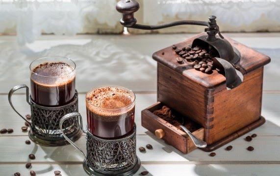 Early coffee wave: Vintage roasting equipment in action with brewed coffee in bronze cups.