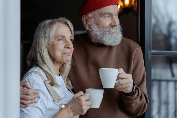 An elderly couple enjoys a cozy moment together, savoring their coffee by the window.