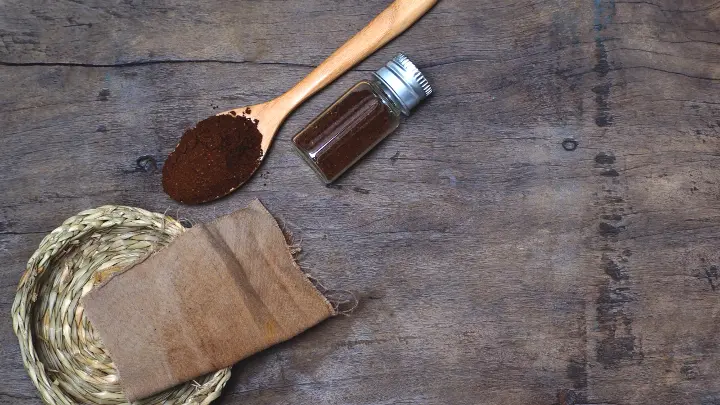 A piece of fabric lays next to a mound of coffee grounds, showcasing the materials for a DIY fabric dye project.