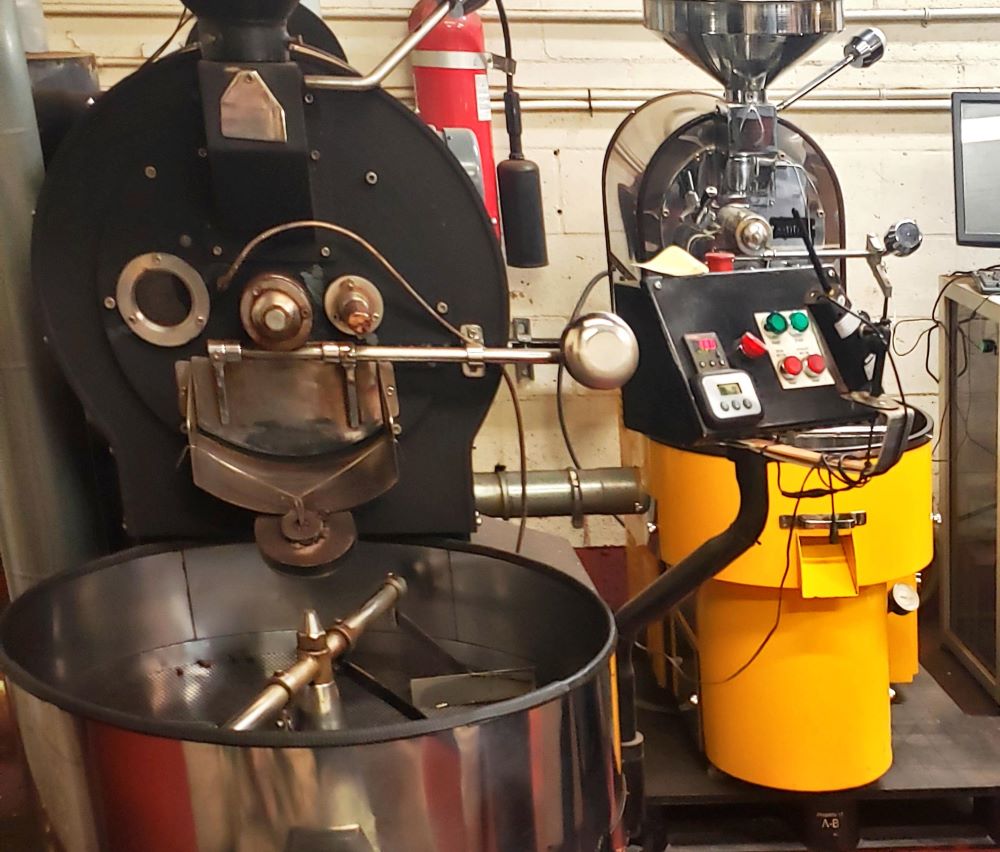 Industrial coffee roaster machine with controls and a rotating drum, ready for roasting coffee beans in a professional setup.
