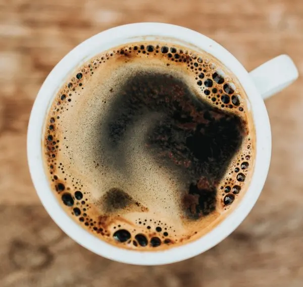 A cup of freshly brewed coffee in a white ceramic cup. The cup is filled with dark, steaming coffee, giving off a rich aroma. The background is simple, focusing on the cup's elegant simplicity and the coffee's inviting appearance.