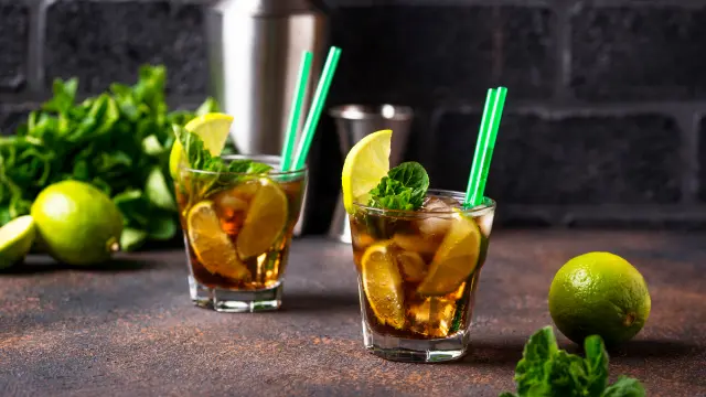 Glasses of iced coffee mojito with fresh mint leaves and lime wedges, filled with ice and sparkling water, placed on a sunlit patio table with a refreshing summer vibe.
