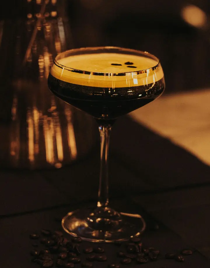 A glass of Café Vino features a blend of dark, chilled coffee and rich Port wine, topped with a sprinkle of cinnamon, set on a cozy wooden table.