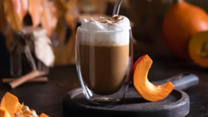 A visually appealing shot of a pumpkin spice latte in a cozy fall setting—think cinnamon sticks, whipped cream, and autumn leaves.