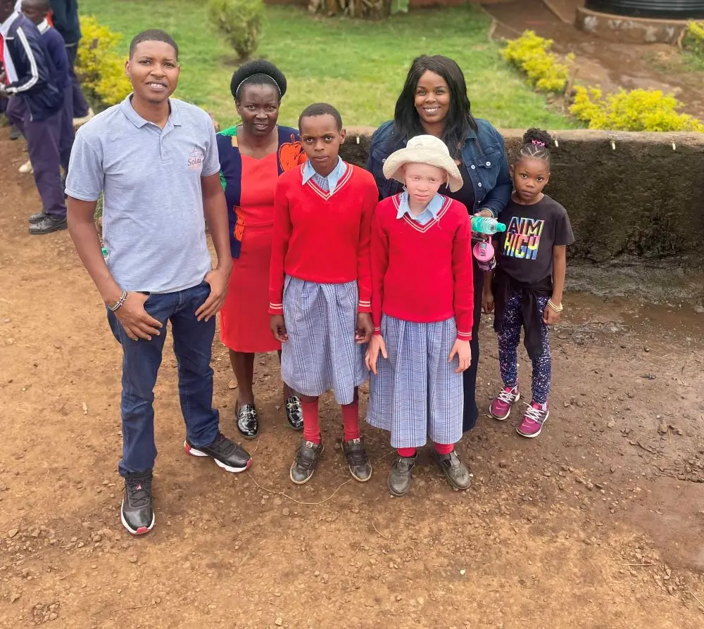 Peter, Monica and their daughter Imani posing for a photo with students Sharom, who is deaf, and Jane, who has albinism, along with their teacher.