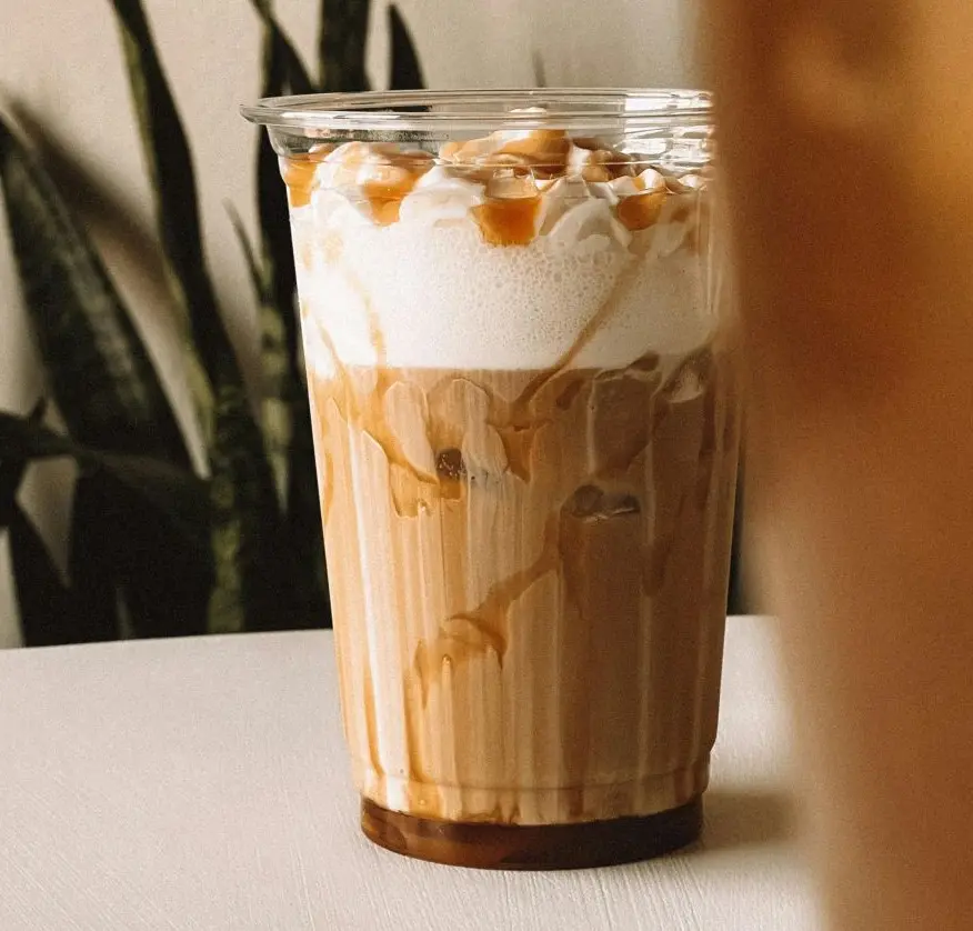A clear recycled glass filled with caramel-infused coffee showcasing a rich, golden hue.