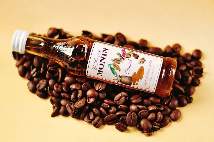 A bottle of coffee syrup placed on a bed of single-origin coffee beans, emphasizing flavor enhancement.
