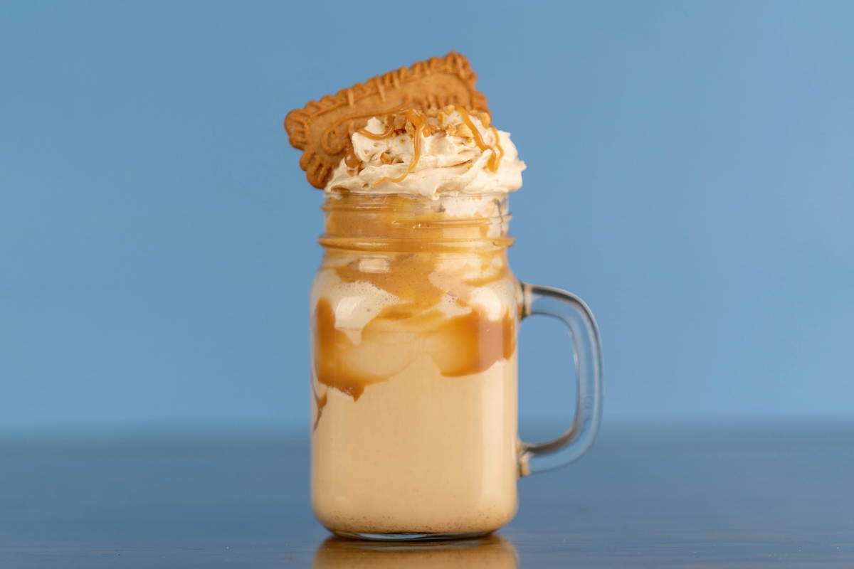 An image of a gingerbread maple latte in a mason mug topped with whipped cream, maple syrup, and gingerbread cookies for a festive touch.