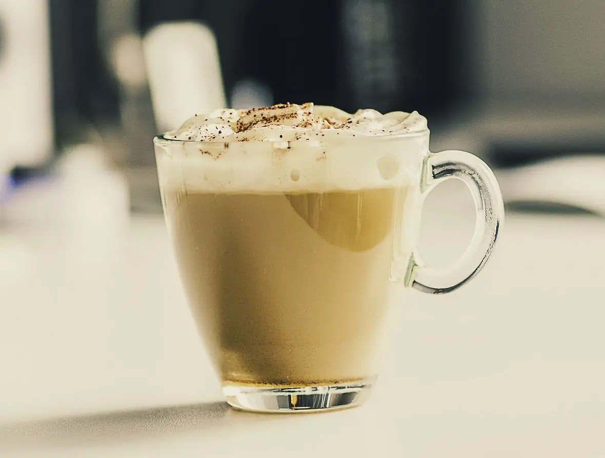 A classic latte topped with whipped cream, a dusting of cinnamon dolce topping, and served in a cozy mug, radiating warm holiday vibes.