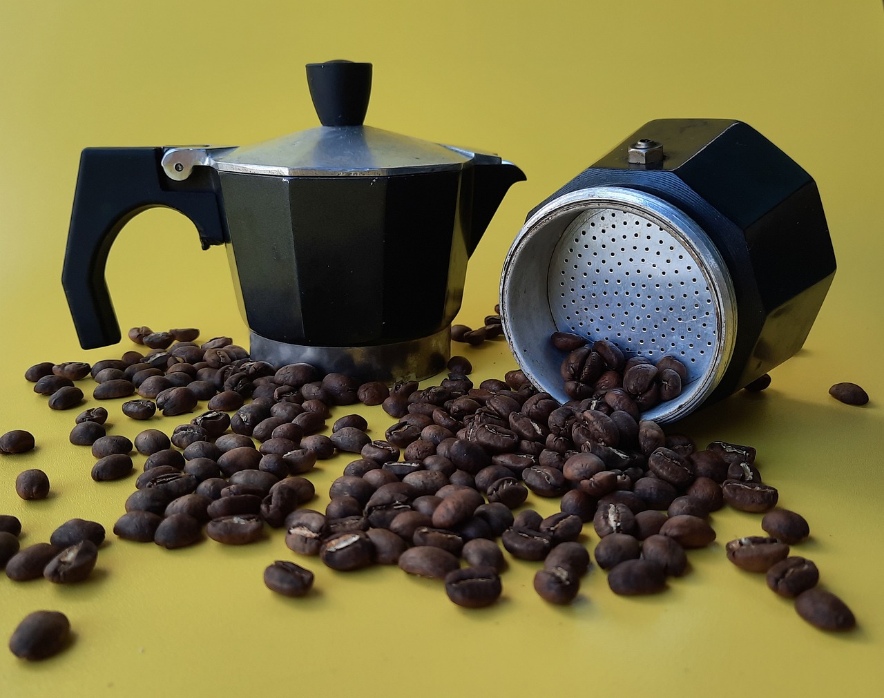 An image of moka pot and dark roast coffee beans on the surface