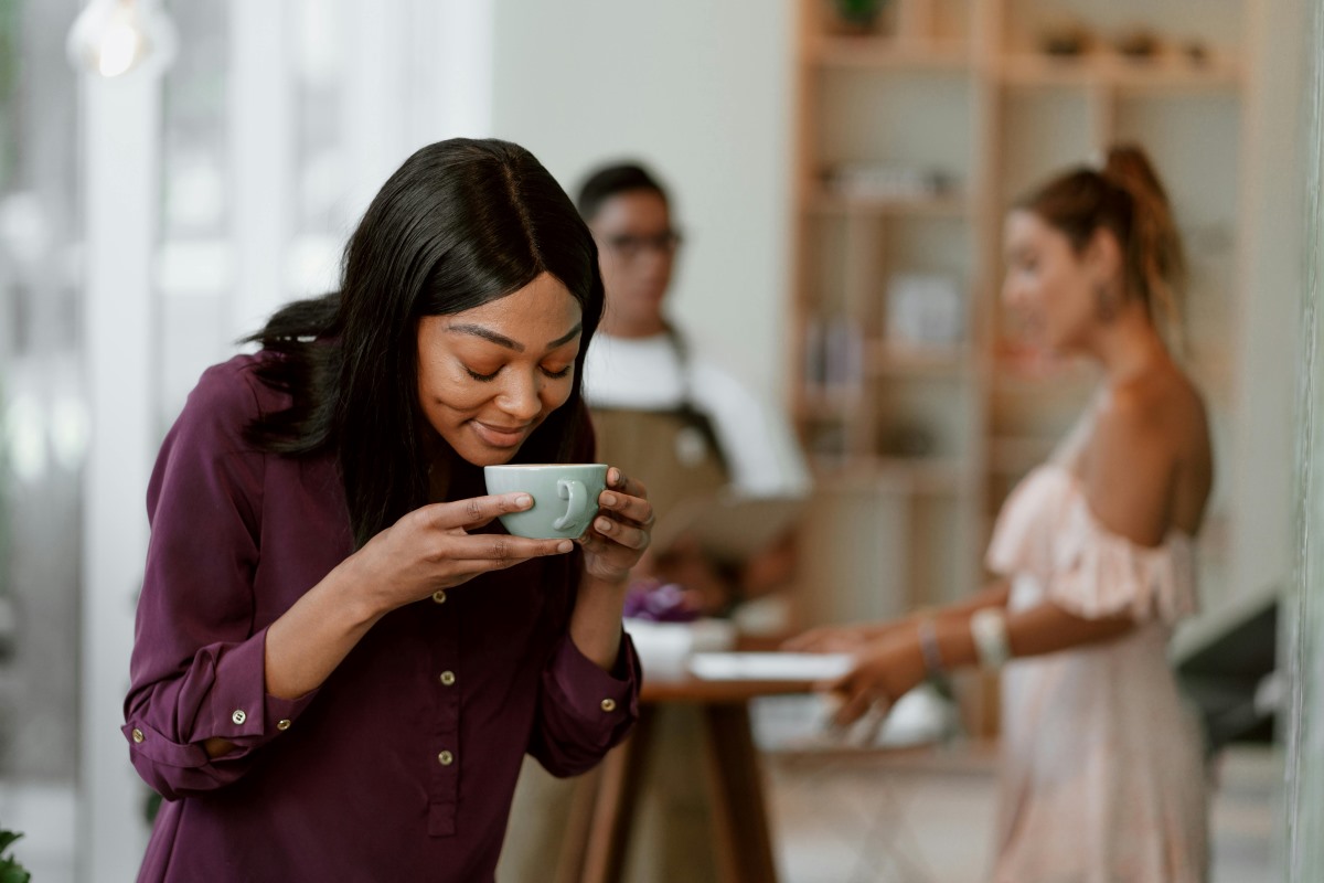 A woman smelling freshly brewed coffee in a white ceramic cup, enjoying the rich aroma and freshness.