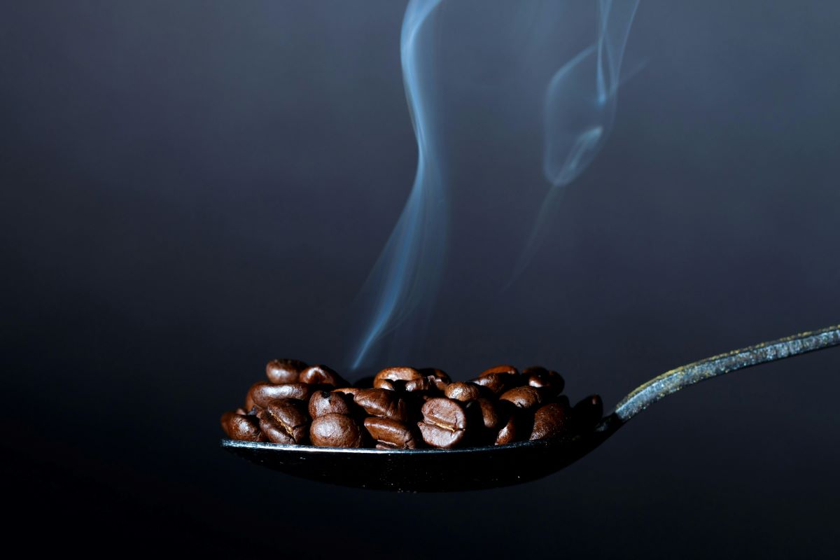 Steaming hot coffee beans on a spoon, with visible steam rising to highlight the aroma and freshness.