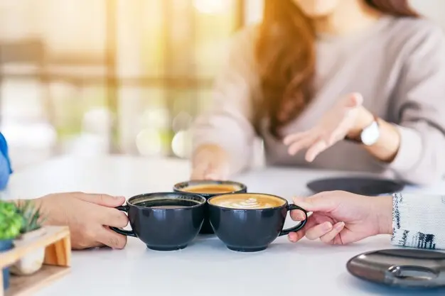 Coffee Gathering Close-up of three people clinking black coffee cups together at a café table, symbolizing connection and community while discussing over coffee.