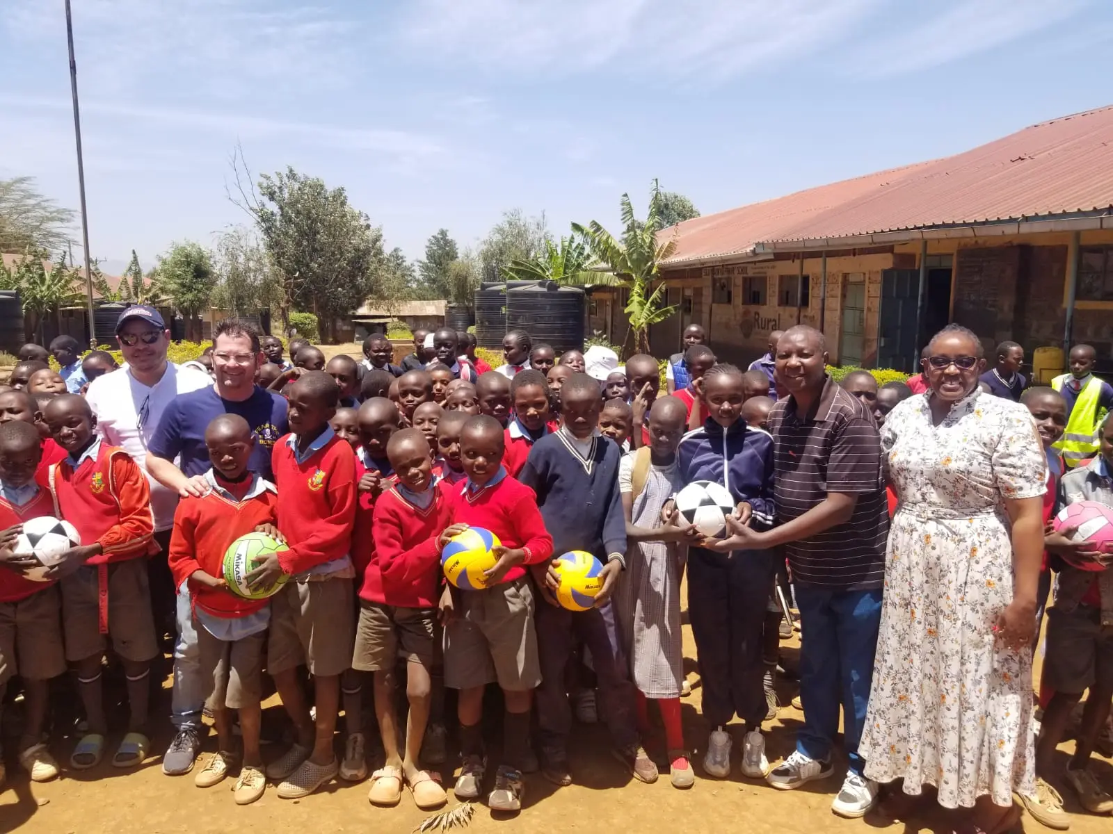 Brad Otto and Marvin Tejada from Acts of Wisdom pose for a photo with teachers and students after presenting soccer balls as gifts, bringing smiles and excitement to the children.