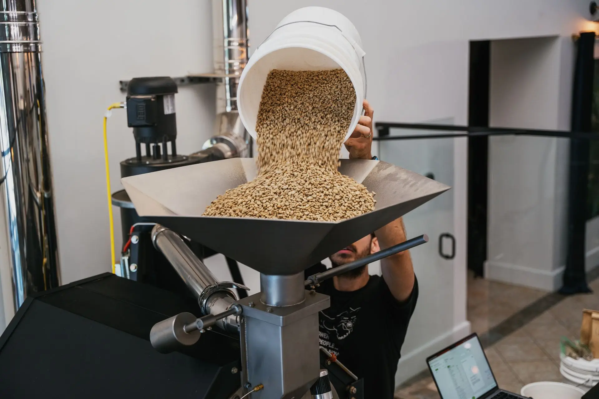 A coffee roaster carefully roasting single-origin coffee beans in a modern roasting machine, showcasing precision and craftsmanship.