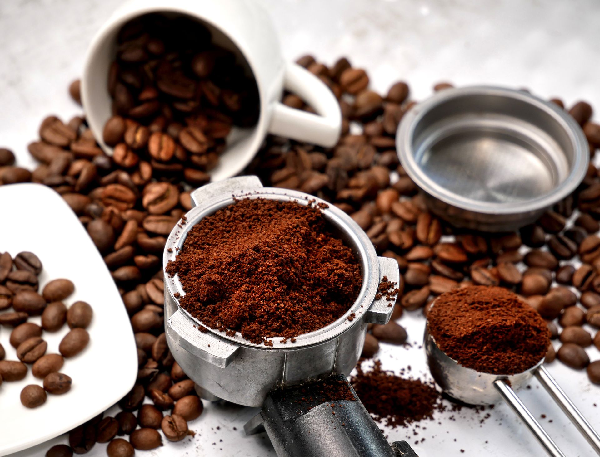 An image showing both roasted coffee beans and grounded coffee in a scoop ready for use